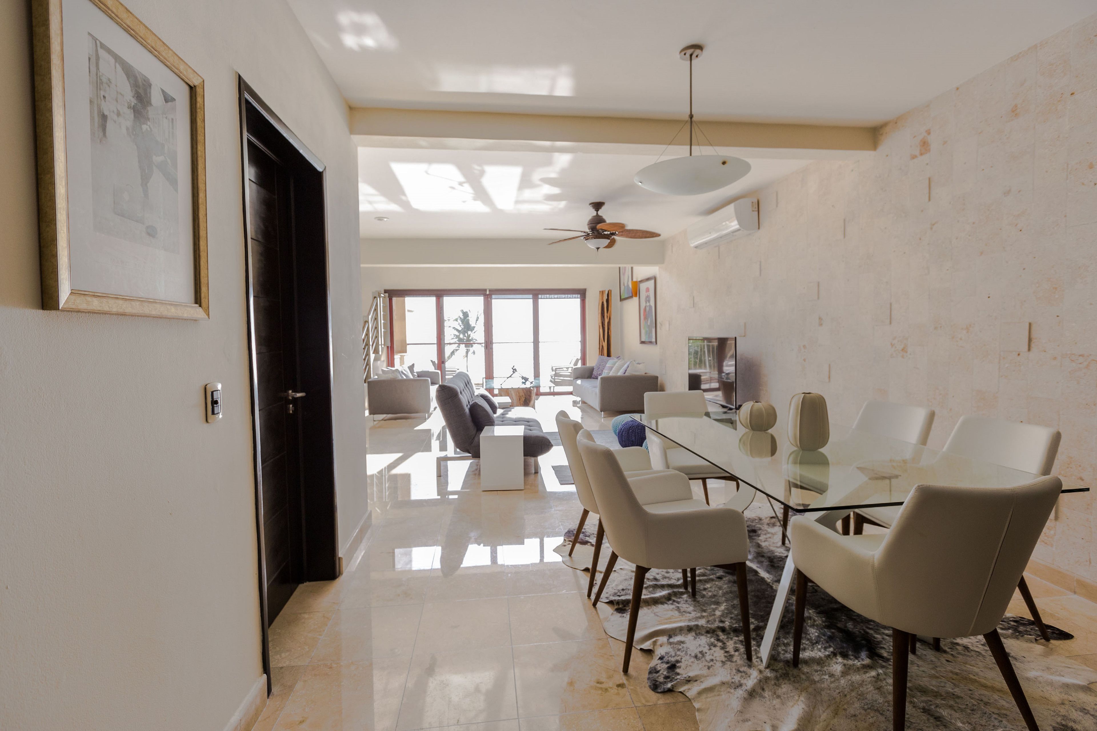 A spacious living area with a glass dining table, modern chairs, and a ceiling fan.
