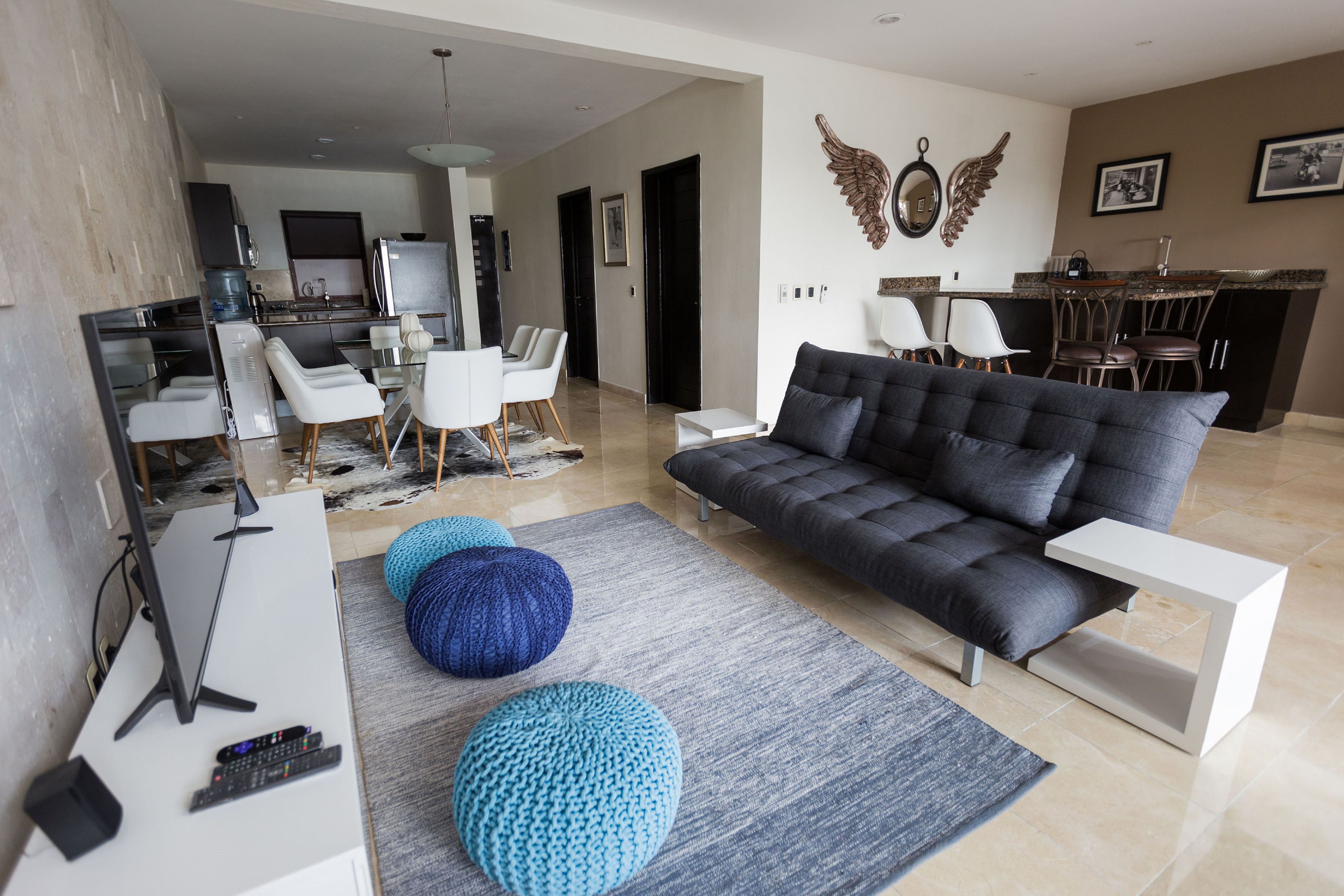 A modern living room with a grey sofa, white chairs, a coffee table, and a TV on a white stand.