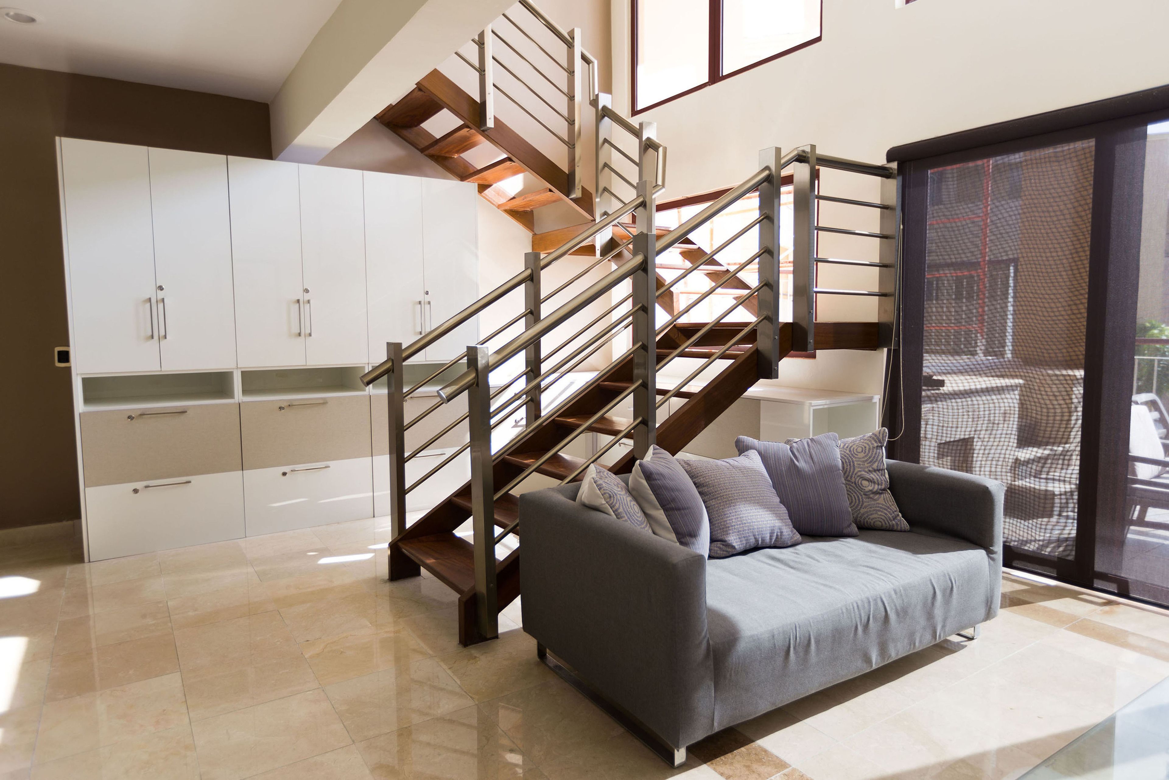 A modern living room with a grey sofa, a wooden staircase, and white cabinets.