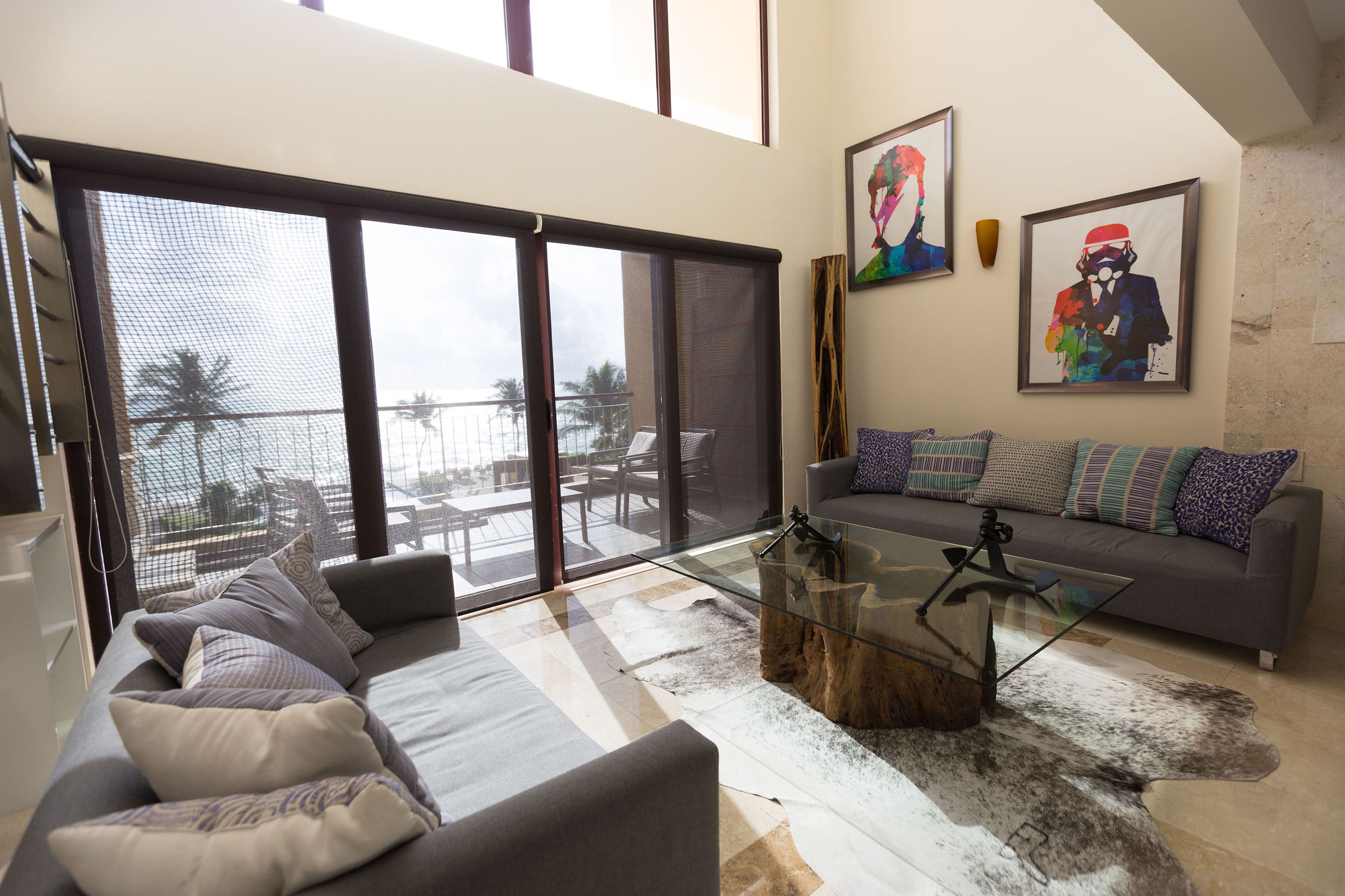 Ein modernes Wohnzimmer mit einem grauen Sofa, einem Glastisch und einer großen Schiebeglasdoor zum Balkon.