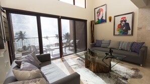 Un salon moderne avec un canapé gris, une table basse en verre et une grande porte-fenêtre coulissante donnant sur un balcon.