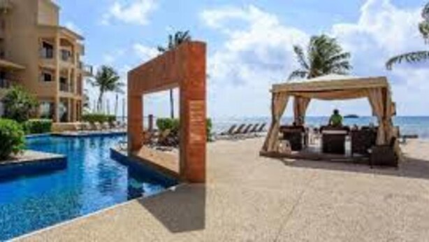 Un espace piscine aménagé dans un complexe hôtelier, avec une piscine à l’eau cristalline, une pergola en bois et un cabanon de plage.
