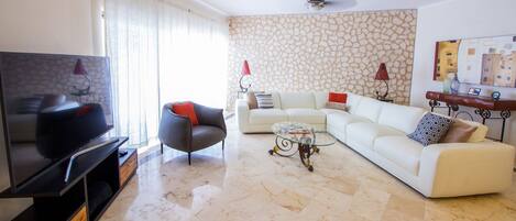 A living room with a flat-screen TV, a sofa, a coffee table, and a stone-patterned wall.