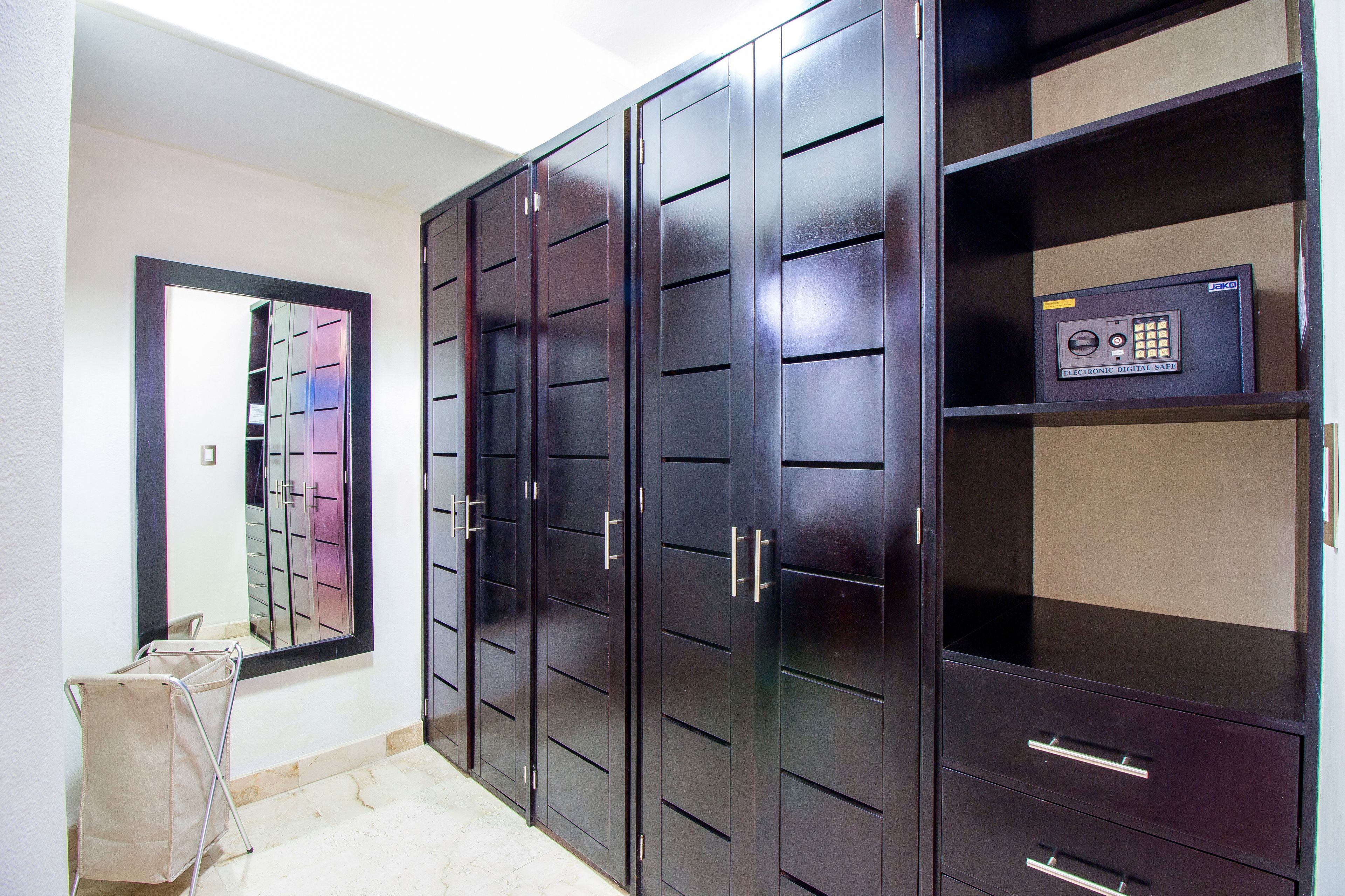 A room with a large wardrobe, a mirror, and a shelf with a safe.
