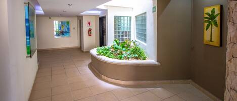 A hallway with a curved planter with plants, a fire extinguisher, and a painting on the wall.