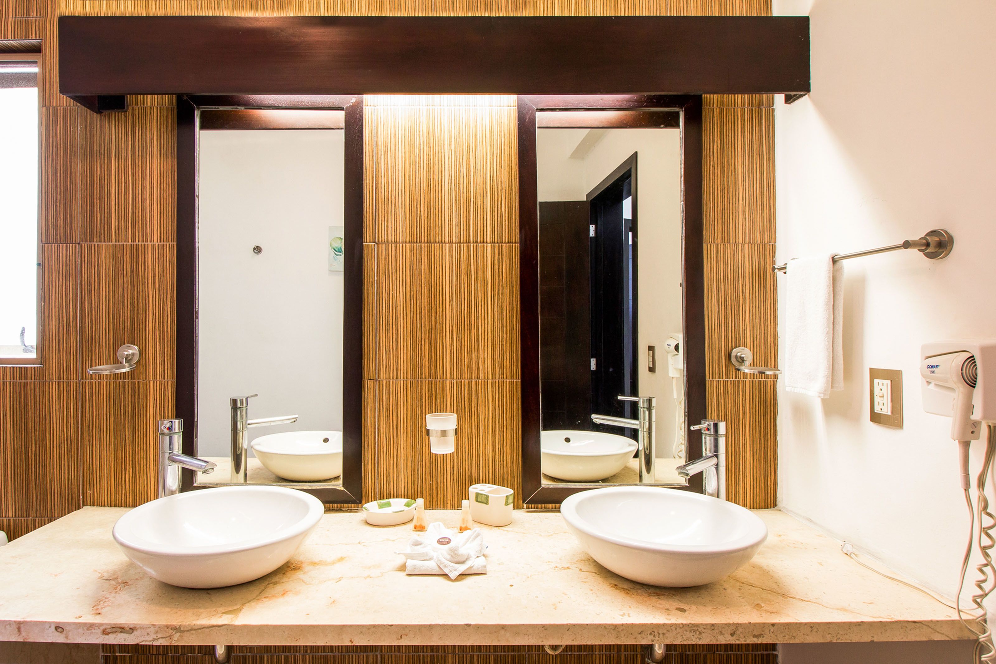 A bathroom with two sinks, a large mirror, and a hairdryer on the wall.