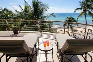 A balcony with two lounge chairs and a small table with two glasses of a beverage. - Oceanfront Condo, 2 Bedrooms, Second Floor at Corto Maltes by DPM (Playa del Carmen)