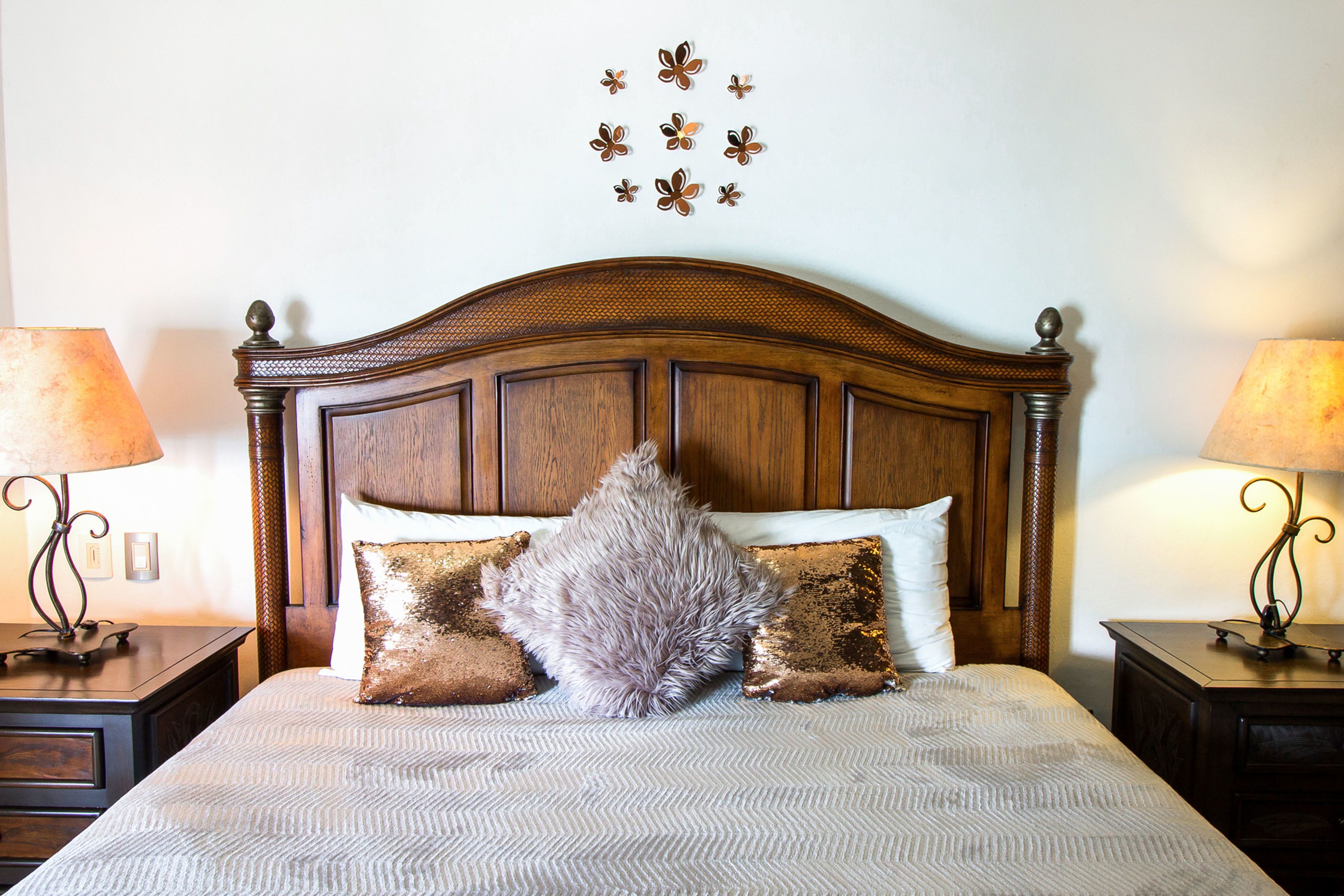 A neatly made bed with a wooden headboard, two bedside tables with lamps, and decorative wall art.