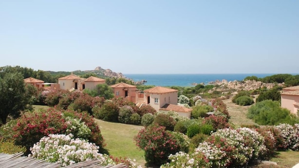 A coastal villa complex with multiple buildings, lush gardens, and a view of the sea.