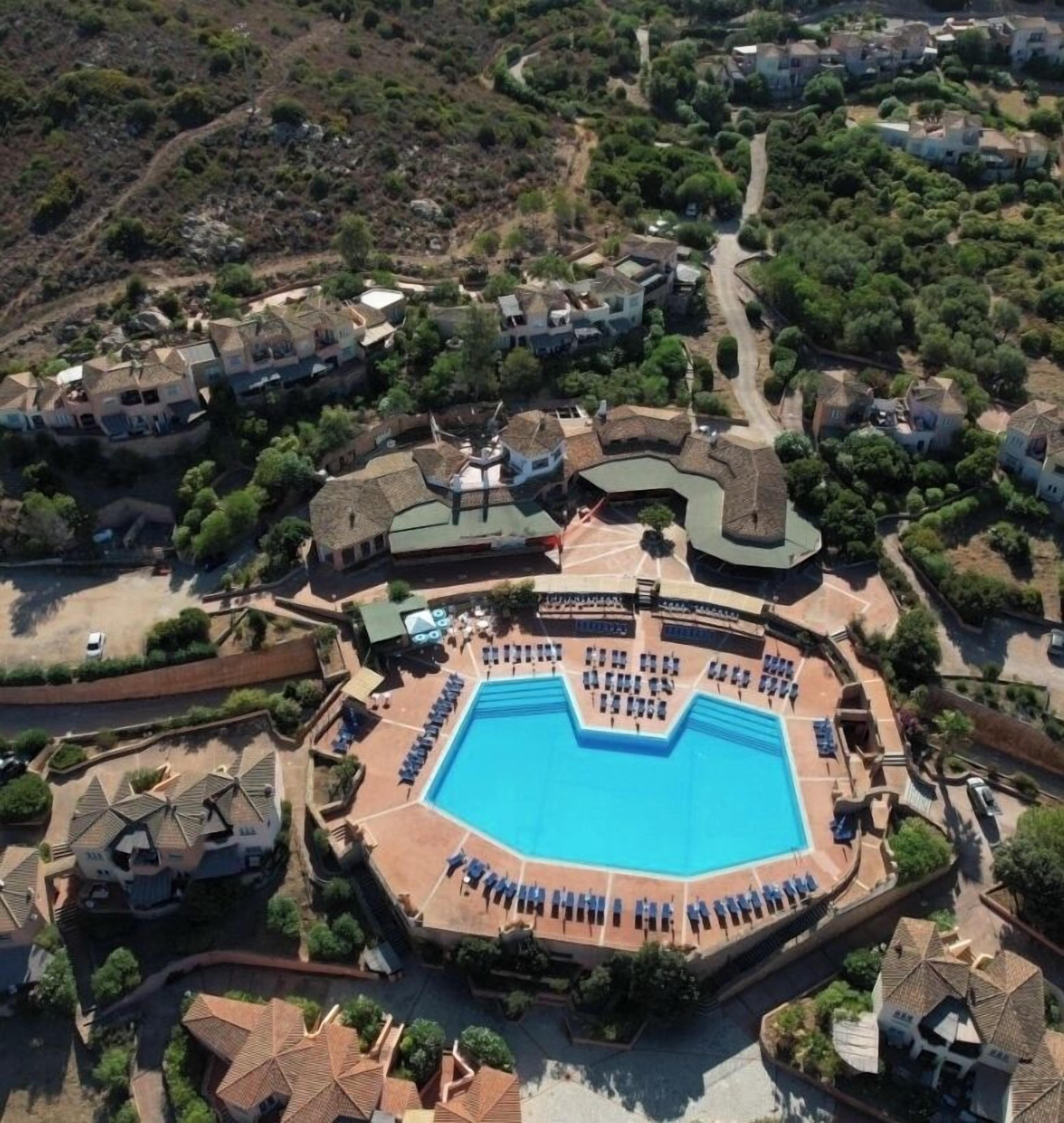 An aerial view of a resort with a central swimming pool, multiple villas, and a well-maintained landscape.