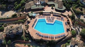 An aerial view of a resort with a central swimming pool, multiple villas, and a well-maintained landscape.