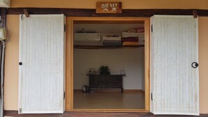 A traditional Japanese room with sliding doors, a shelf with folded textiles, and a small table with a plant.