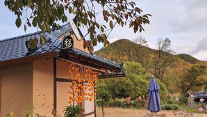 A traditional building with a tiled roof, a hanging orange decoration, and a garden with flowers and a bench.