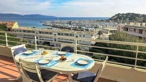 A balcony with a table set for two, overlooking a marina and coastal town. - Nice apartment for 6 people with WIFI, A/C, pool, TV and terrace (Cavalaire-sur-mer)