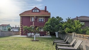A two-story house with a red-tiled roof, a small balcony, and a well-maintained lawn with lounge chairs. - Villa on the coast Santander (Monte - Santander)