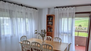 A dining area with a wooden table and white chairs, a bookshelf, and a view of a green landscape through a glass door. - Villa on the coast Santander (Monte - Santander)
