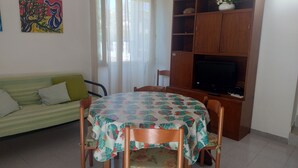 A living room with a sofa, a dining table with chairs, a TV on a wooden cabinet, and a painting on the wall. - GROUND FLOOR APARTMENT WITH CALA GONONE VERANDA AT 30 MT FROM THE SEA (Cala Gonone)