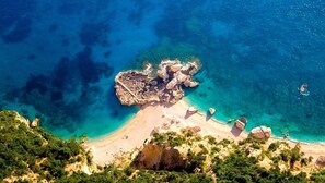Vista aérea de una zona costera con aguas turquesas cristalinas, formaciones rocosas y una playa de arena.