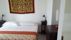 A bedroom with a bed, a nightstand, a dresser, a wall tapestry, and a door. - GROUND FLOOR APARTMENT WITH CALA GONONE VERANDA AT 30 MT FROM THE SEA (Cala Gonone)