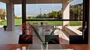 Un coin repas avec une table dressée pour deux personnes, une vue dégagée sur l’extérieur grâce à de grandes fenêtres et une plante en pot posée sur la table.