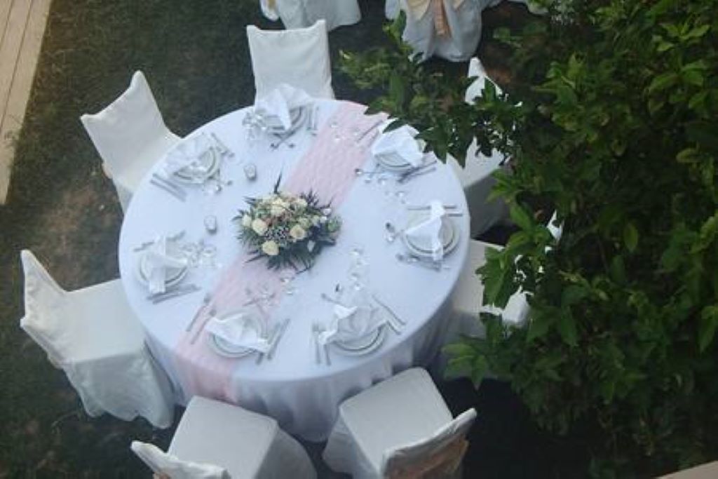 Ett runt bord dukat för sex personer, med vita stolar, en rosa bordslöpare och en blomsterdekoration i mitten.