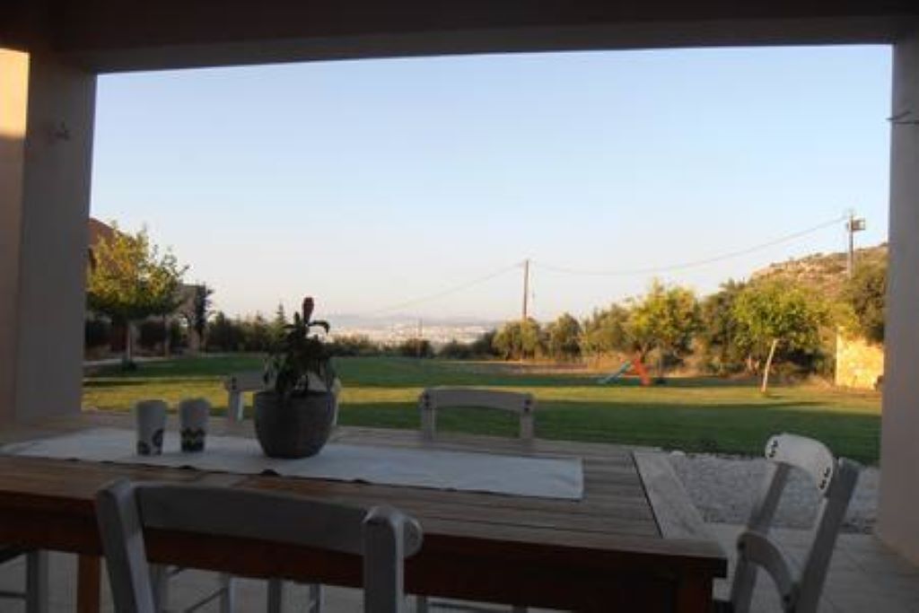 A patio with a table and chairs, a potted plant, and a view of a grassy area and hills.