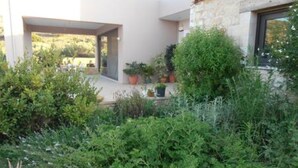 Il s’agit d’un bâtiment moderne à l’extérieur blanc et doté d’une façade en pierre. Devant le bâtiment, on trouve des plantes en pot et un petit espace aménagé en jardin.