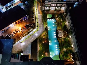 Nachtsichtaufnahme eines Hotels mit Schwimmbad, Parkplatz und angrenzenden Gebäuden.