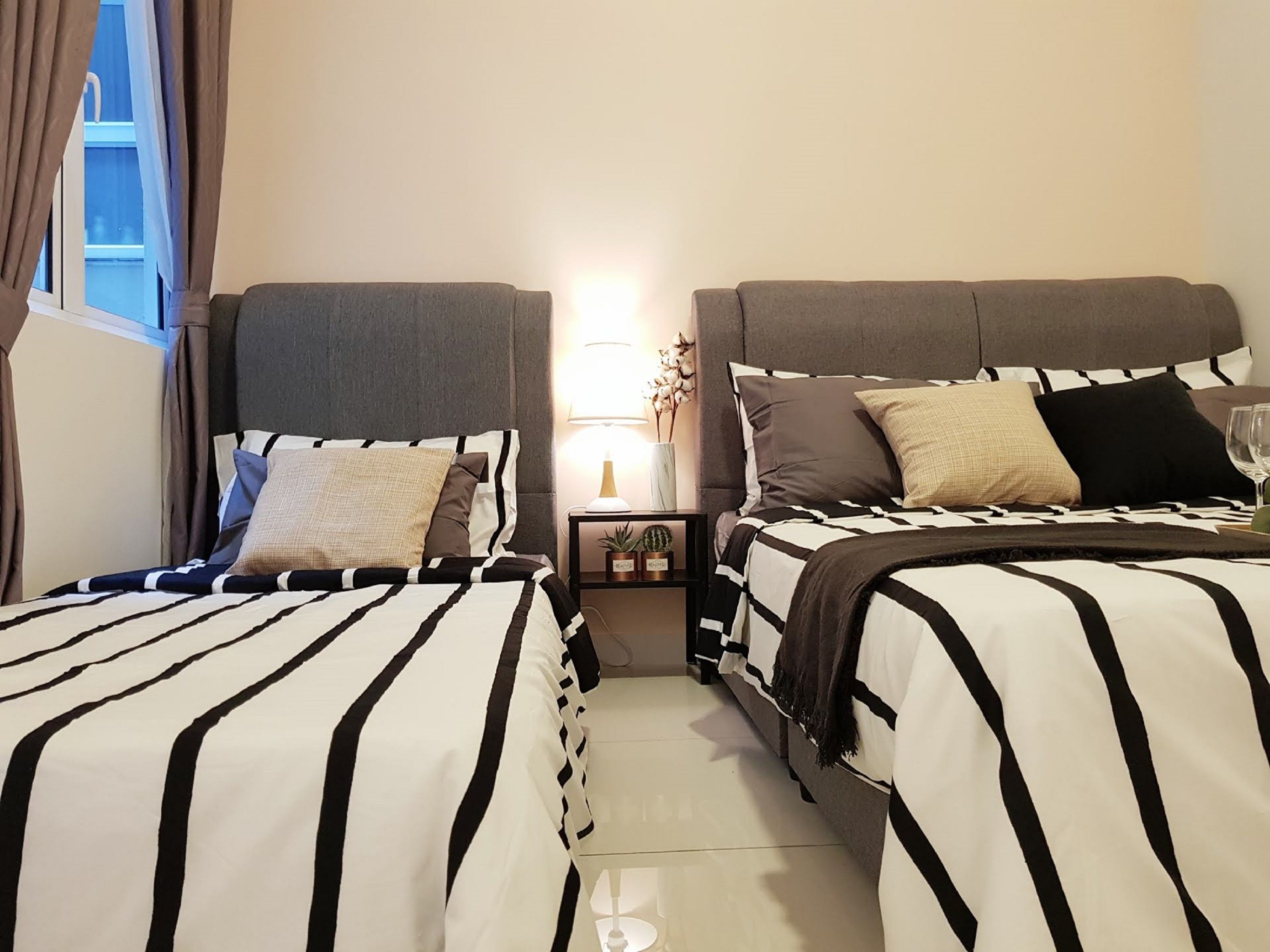 Une chambre d’hôtel avec deux lits, chacun doté de draps à rayures, une table de chevet avec une lampe et une petite plante.