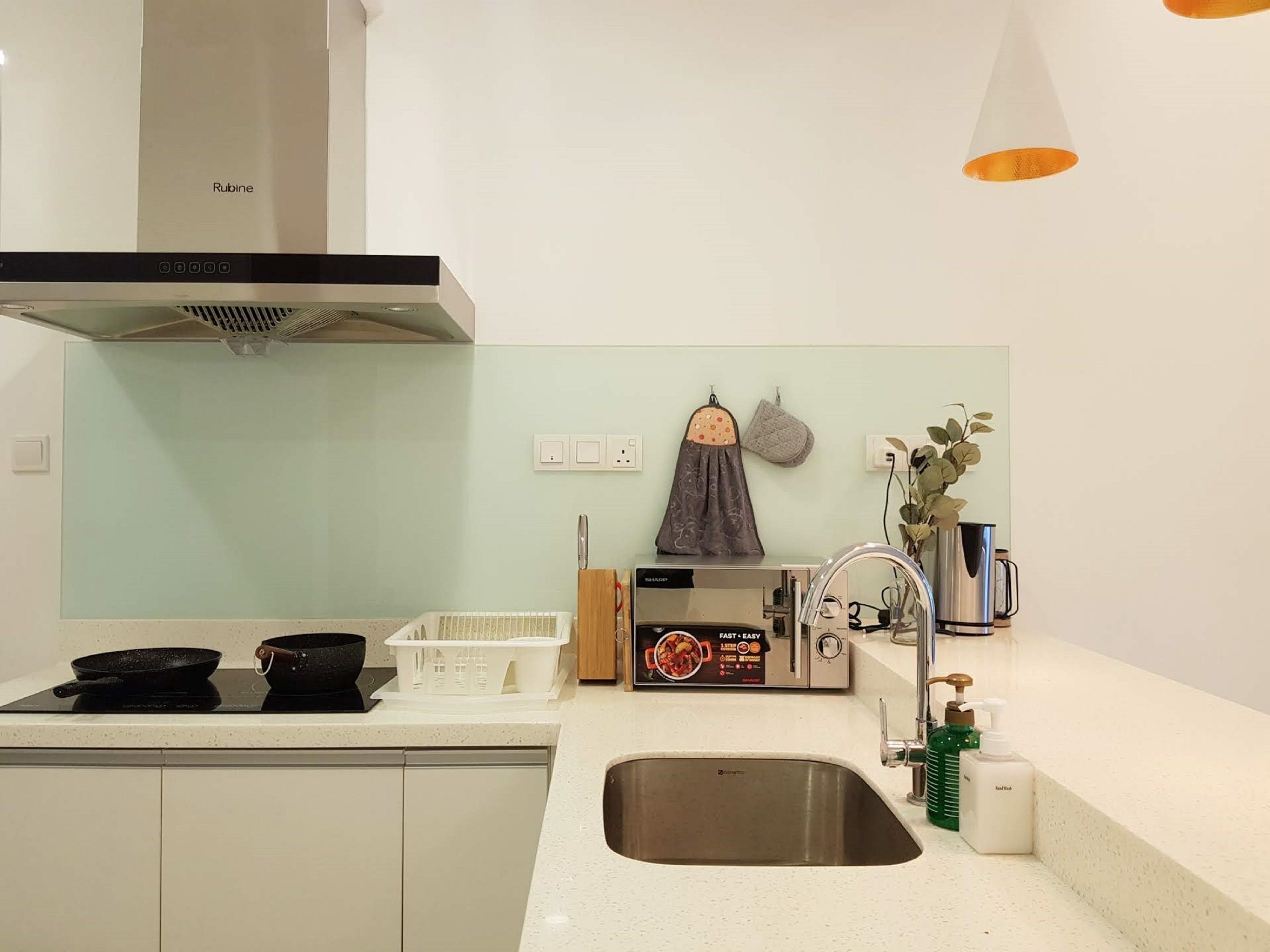 A modern kitchen with a stainless steel sink, a range hood, and a countertop with a kettle and a dish rack.