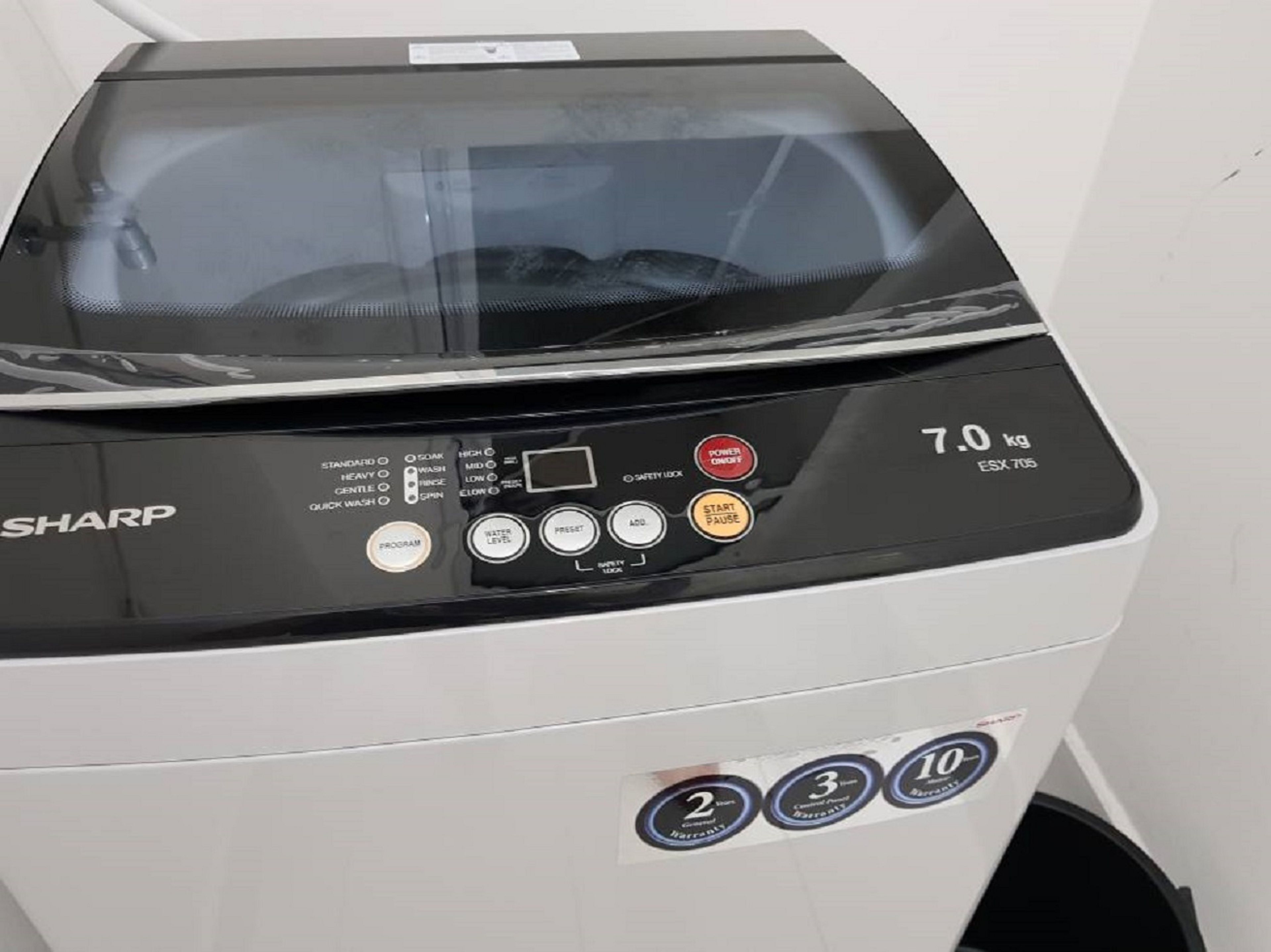 A front view of a white Sharp washing machine with a digital display, control buttons, and a weight capacity indicator of 7.0 kg.