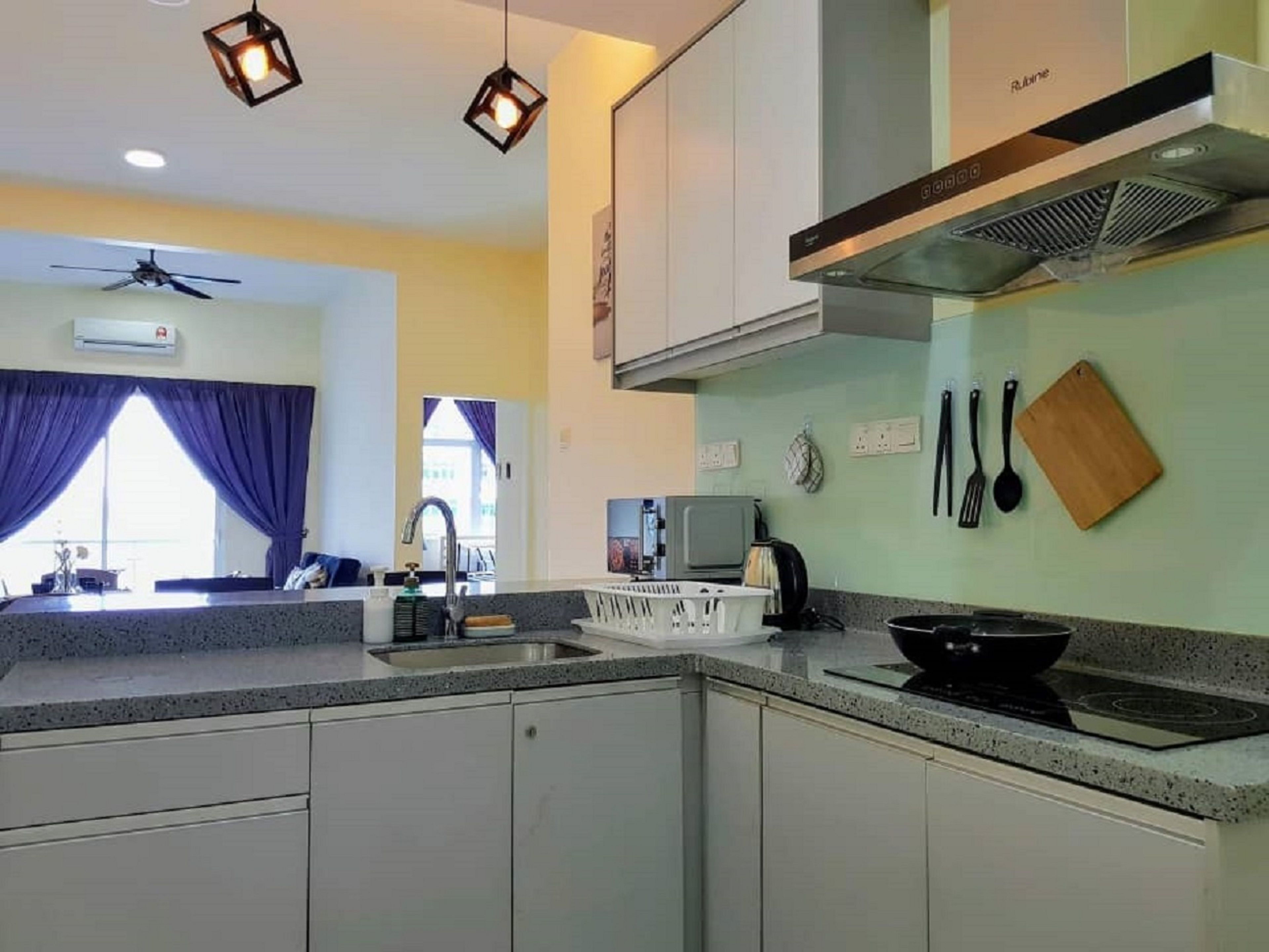Una cocina moderna con armarios blancos, estufa a gas y campana extractora. Hay luces colgantes, ventilador de techo y una ventana con cortinas.