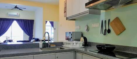 Una cocina moderna con armarios blancos, estufa a gas y campana extractora. Hay luces colgantes, ventilador de techo y una ventana con cortinas.