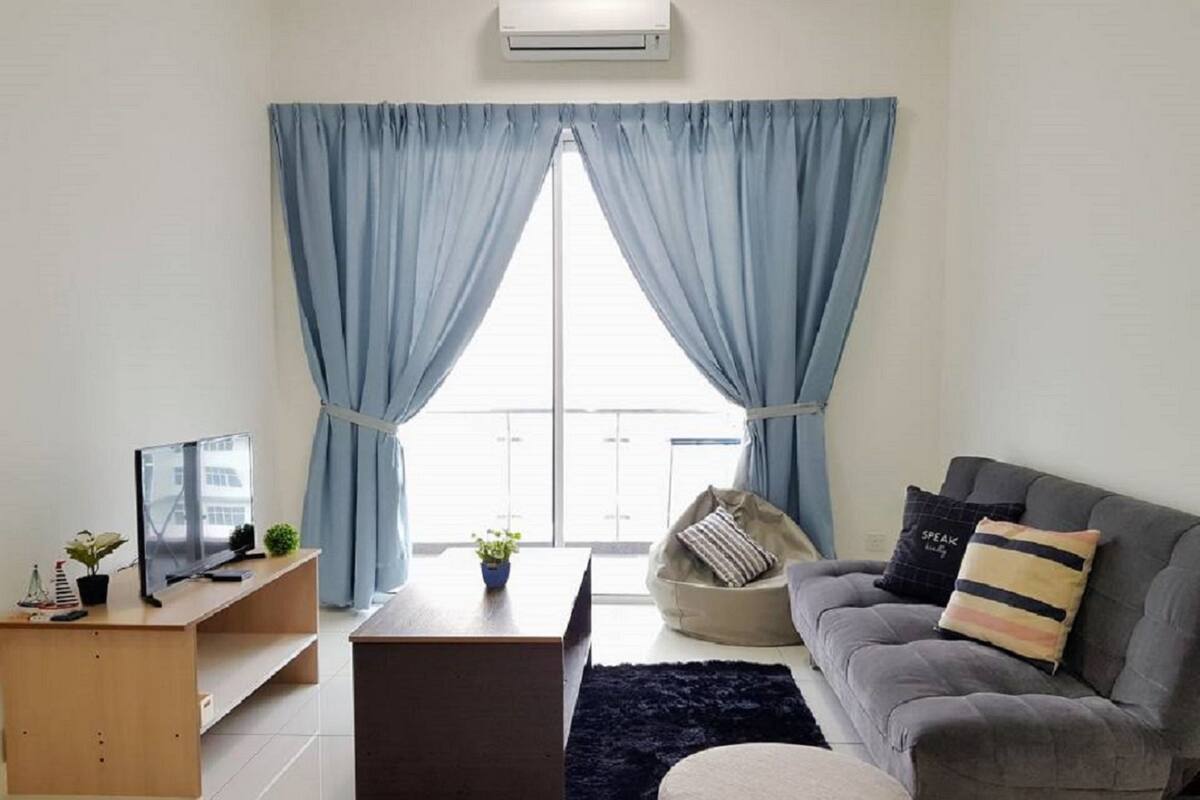 Ein modernes Wohnzimmer mit einem grauen Sofa, einem Holztisch und einem Fernseher auf einem Standfuß. Ein großes Fenster mit blauen Vorhängen, eine Topfpflanze und ein schwarzer Teppich sind ebenfalls vorhanden.