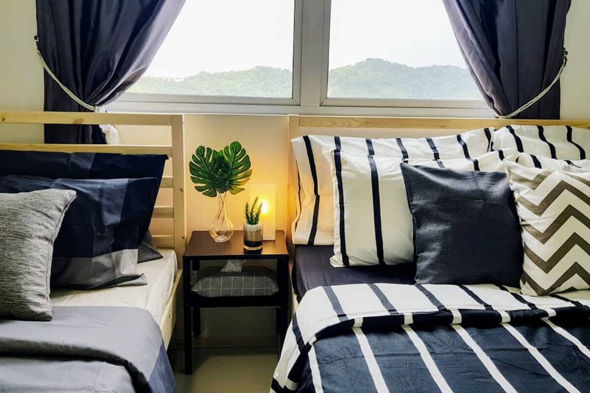 Ein Zimmer mit zwei Betten, einem Nachttisch mit Pflanze und einem Fenster mit Vorhängen.