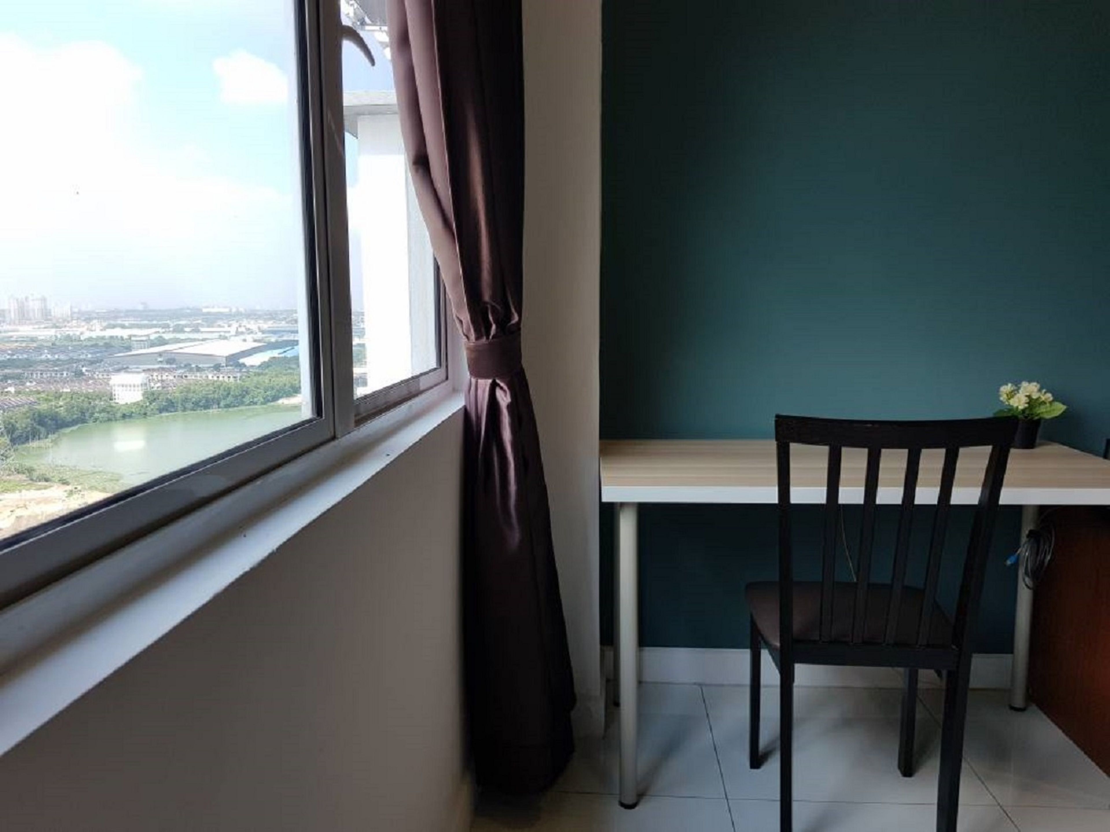 A room with a view of a river and cityscape through a window, a wooden chair, and a table with a potted plant.