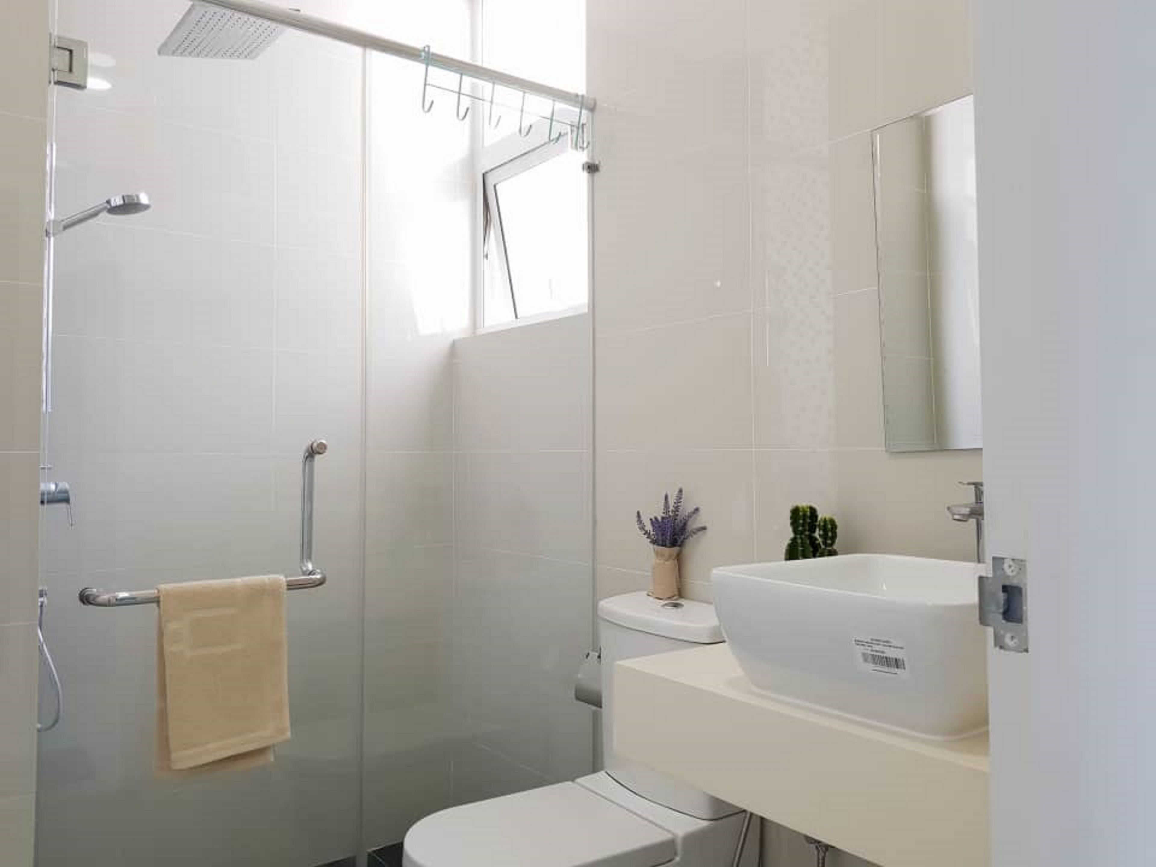 Une salle de bain moderne avec une douche à parois de verre, des toilettes blanches, un lavabo avec un miroir et une petite plante en pot.