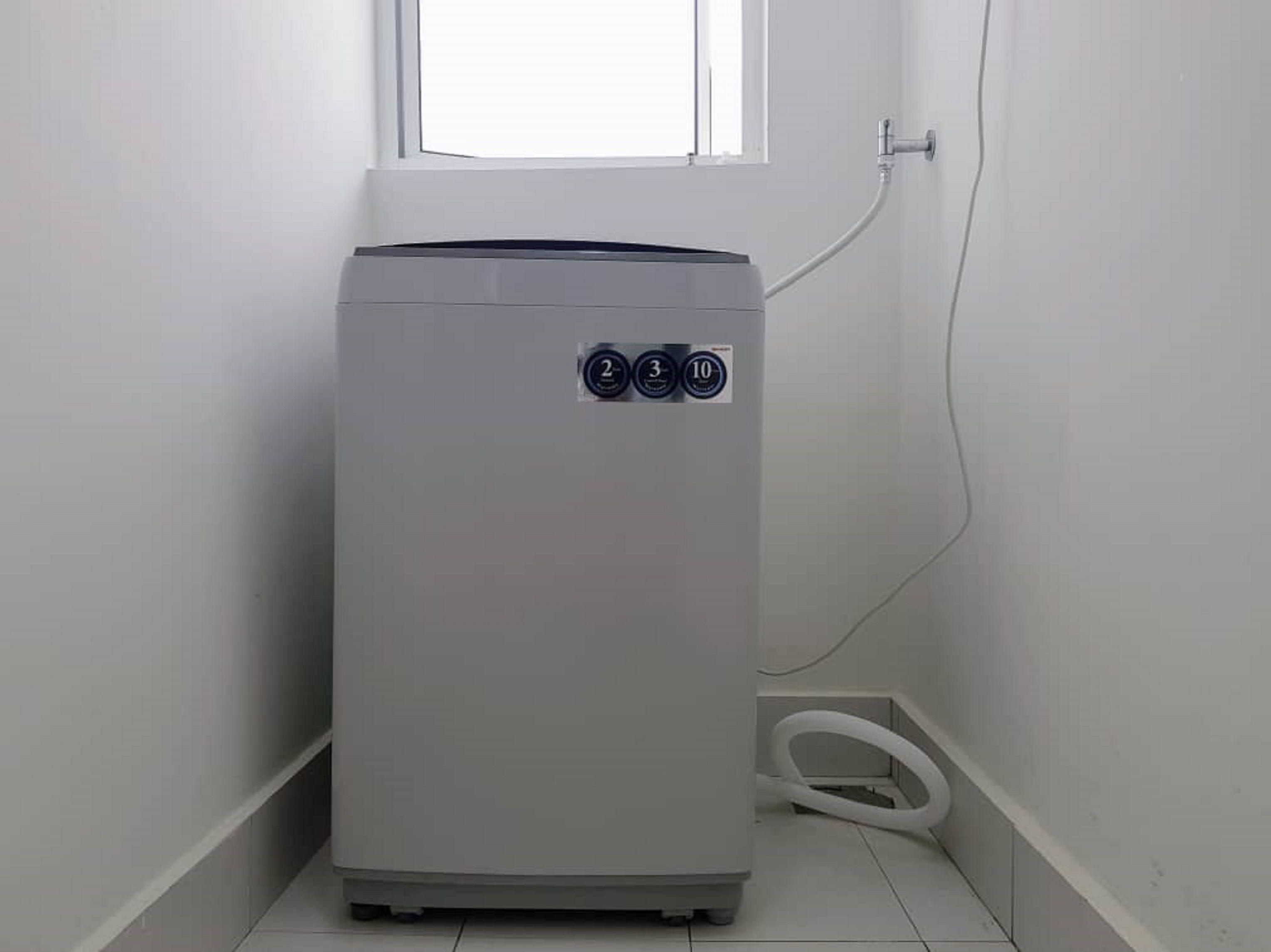 A compact, white water heater in a corner with a window above it.