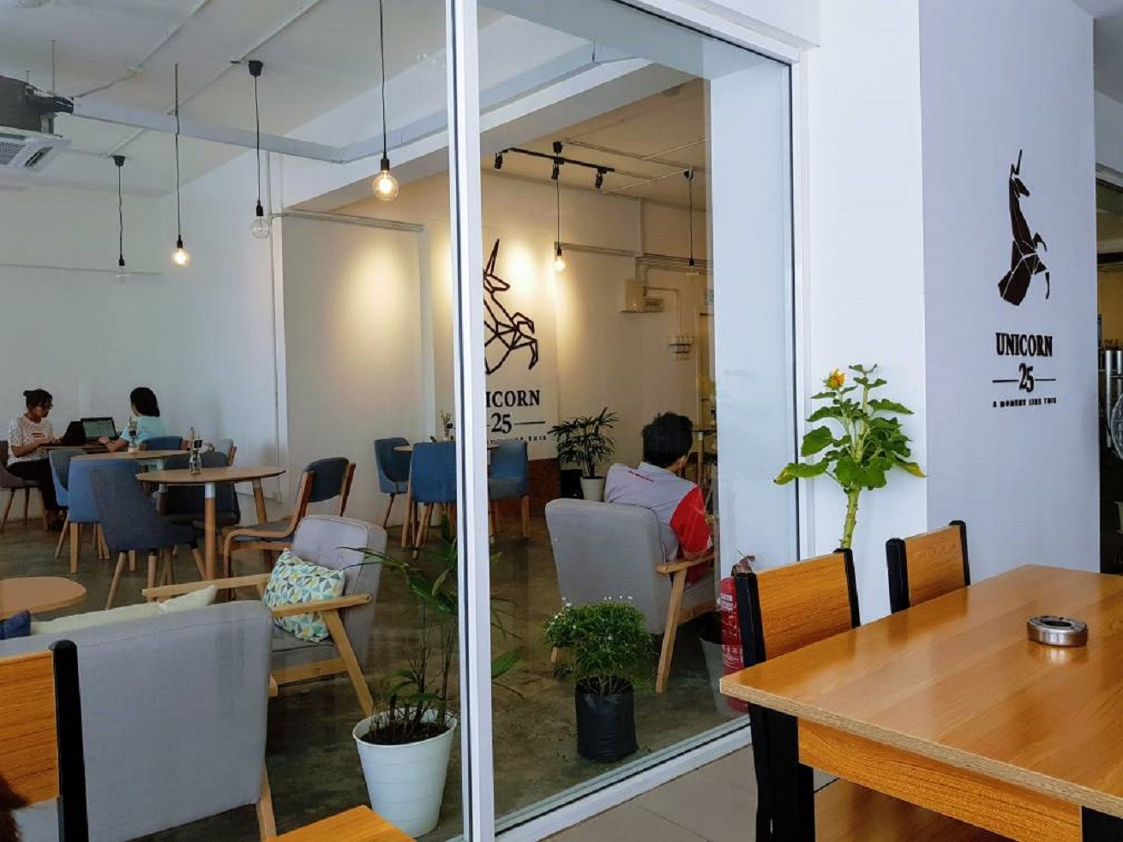 Un café moderno con mesas y sillas de madera, un muro de cristal y un mural de unicornio.
