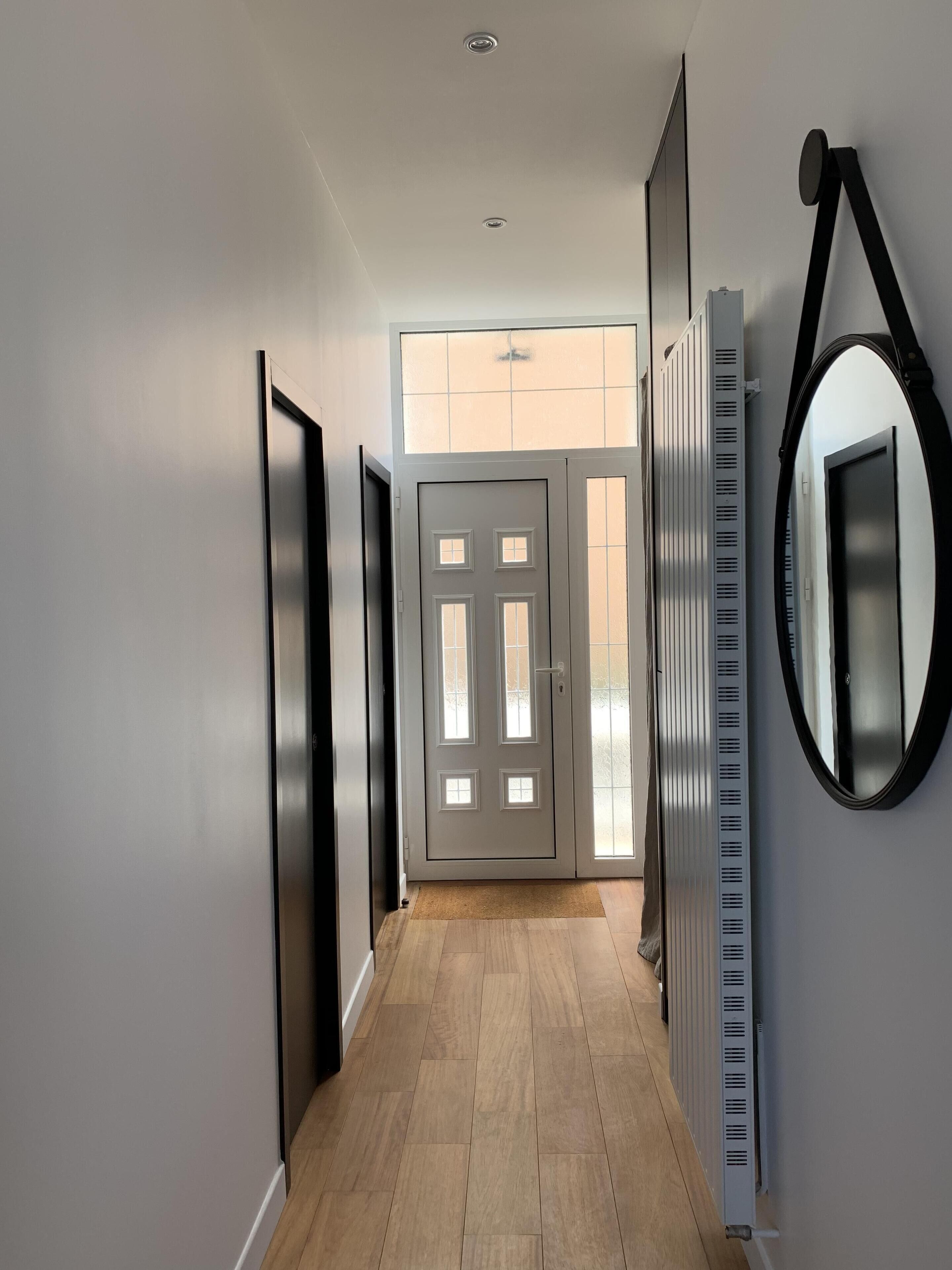 Un couloir avec un plancher en bois, une porte blanche dotée de panneaux de verre et un radiateur sur le côté droit.