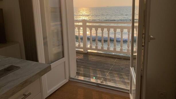 A room with a view of the ocean at sunset through a glass door.