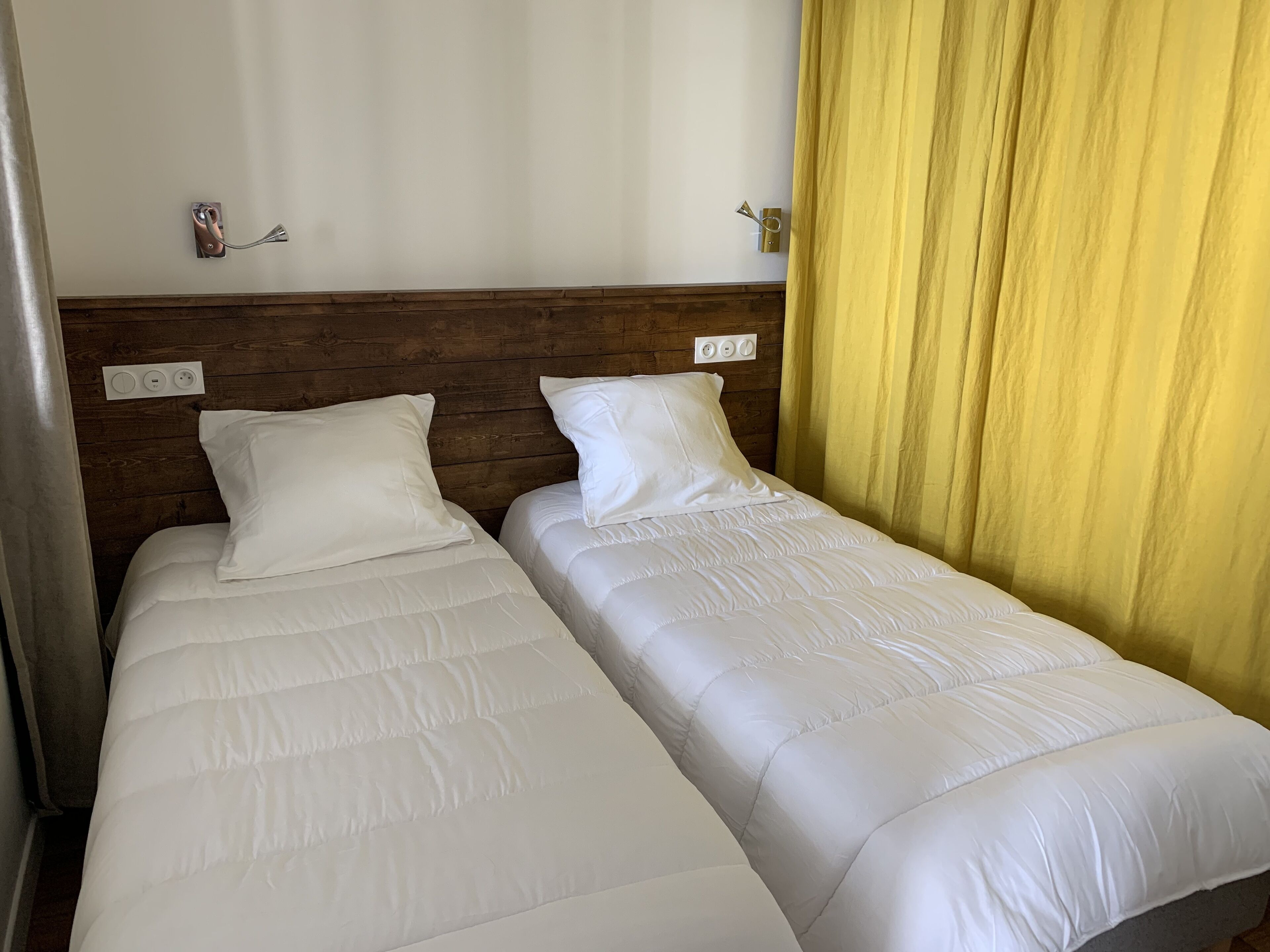 Two single beds with white bedding, wooden headboard, and a yellow curtain.