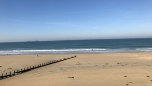 A wide sandy beach with a wooden fence running parallel to the shore.