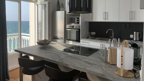 A modern kitchen with a large island, stainless steel appliances, and a view of the sea.