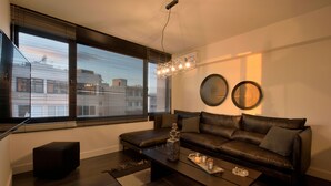 Ein modernes Wohnzimmer mit einem dunkelbraunen Ledersofa, einem Glastisch und einem großen Fenster mit Jalousien.