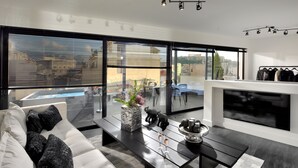 Ein modernes Wohnzimmer mit Sofa, Couchtisch und Kamin. Große Fenster bieten Blick auf die Stadt und einen Pool.