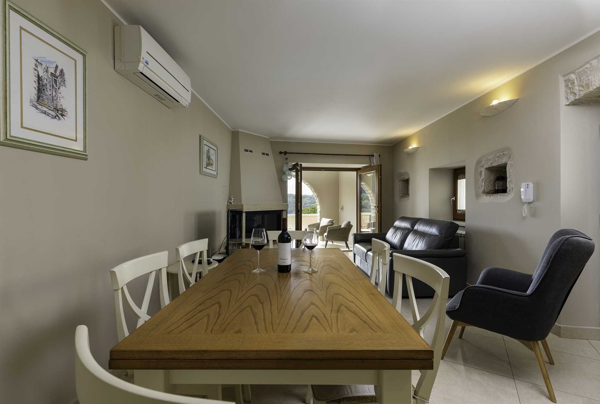 A dining area with a wooden table and white chairs, a black leather sofa, and a fireplace.