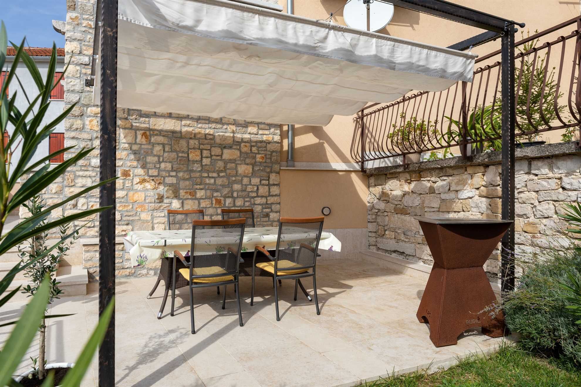 Une terrasse extérieure avec un mur en pierre, une table avec des chaises et un grand bac à fleurs.