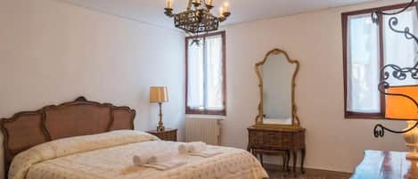 A bedroom with a large bed, a chandelier, a mirror, and a dresser.