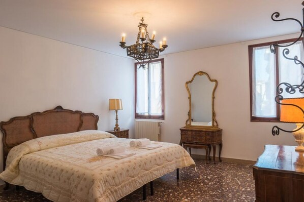 A bedroom with a large bed, a chandelier, a mirror, and a dresser.